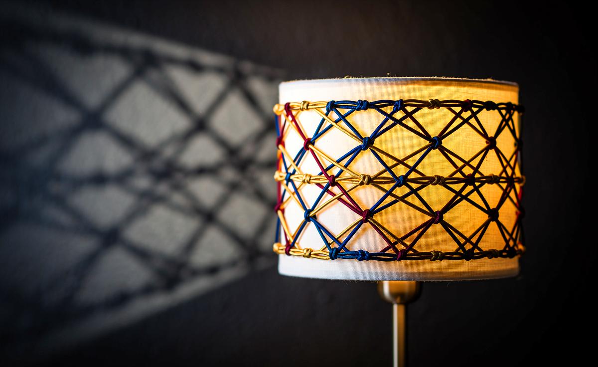 Illustration von einer Lampe mit einem Schirm, der durch kunstvoll arrangierte Haargummis ein strukturiertes Lichtmuster an die Wand wirft.